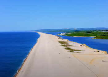 Aerial View of Chesil Beach An aerial view showcasing the expansive panorama of Chesil Beach on the Jurassic Coast. The turquoise ocean seamlessly blends with the sky, framed by unique sands and medieval landscapes. The iconic natural landmarks Durdle Door, Dungy Head, and Man o' War Beach are visible, highlighting the immense potential of nearby properties. Coastal Gem with Medieval Backdrop A drone-captured image of Chesil Beach, emphasizing its unique sands and impressive length. The beach is bordered by medieval landscapes and authentic British architecture, illustrating the harmony between nature and the built environment. Harmonious Blend of Nature and Architecture Aerial footage capturing the seamless blend of traditional British architecture with the rugged beauty of the Jurassic Coast. Quaint cottages and modern beachfront villas harmonize with the surrounding landscape, emphasizing craftsmanship and attention to detail. Inviting Coastal Lifestyle Drone imagery depicting the inviting coastal lifestyle of Chesil Beach. Scenic visuals evoke a sense of adventure and relaxation, with opportunities for water sports and serene seaside living. The image captures the vibrant community and idyllic surroundings. Transformative Aerial Cinematography A dynamic aerial shot showcasing the transformative power of drone cinematography in property marketing. The engaging visuals highlight the unique appeal of Chesil Beach properties, setting new standards in real estate promotion. Discovering Hidden Gems A high-fidelity drone image revealing secluded spots and serene corners of Chesil Beach. The exclusive glimpses promise privacy and tranquility amidst the breathtaking landscape, enhancing the appeal of nearby properties. Invitation to Explore Chesil Beach An inviting aerial view of Chesil Beach, drawing viewers to explore further. The drone footage captures the allure of the coastline, the charm of the architecture, and the vibrant lifestyle, offering a gateway to a new way of living. Slice of British Paradise A cinematic aerial shot of Chesil Beach, presenting it as a piece of paradise. The image showcases the harmonious coexistence of history, nature, and modern luxury, inviting potential buyers to envision a life infused with the beauty and tranquility of the British seaside.