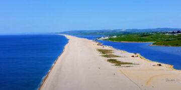 Aerial View of Chesil Beach An aerial view showcasing the expansive panorama of Chesil Beach on the Jurassic Coast. The turquoise ocean seamlessly blends with the sky, framed by unique sands and medieval landscapes. The iconic natural landmarks Durdle Door, Dungy Head, and Man o' War Beach are visible, highlighting the immense potential of nearby properties. Coastal Gem with Medieval Backdrop A drone-captured image of Chesil Beach, emphasizing its unique sands and impressive length. The beach is bordered by medieval landscapes and authentic British architecture, illustrating the harmony between nature and the built environment. Harmonious Blend of Nature and Architecture Aerial footage capturing the seamless blend of traditional British architecture with the rugged beauty of the Jurassic Coast. Quaint cottages and modern beachfront villas harmonize with the surrounding landscape, emphasizing craftsmanship and attention to detail. Inviting Coastal Lifestyle Drone imagery depicting the inviting coastal lifestyle of Chesil Beach. Scenic visuals evoke a sense of adventure and relaxation, with opportunities for water sports and serene seaside living. The image captures the vibrant community and idyllic surroundings. Transformative Aerial Cinematography A dynamic aerial shot showcasing the transformative power of drone cinematography in property marketing. The engaging visuals highlight the unique appeal of Chesil Beach properties, setting new standards in real estate promotion. Discovering Hidden Gems A high-fidelity drone image revealing secluded spots and serene corners of Chesil Beach. The exclusive glimpses promise privacy and tranquility amidst the breathtaking landscape, enhancing the appeal of nearby properties. Invitation to Explore Chesil Beach An inviting aerial view of Chesil Beach, drawing viewers to explore further. The drone footage captures the allure of the coastline, the charm of the architecture, and the vibrant lifestyle, offering a gateway to a new way of living. Slice of British Paradise A cinematic aerial shot of Chesil Beach, presenting it as a piece of paradise. The image showcases the harmonious coexistence of history, nature, and modern luxury, inviting potential buyers to envision a life infused with the beauty and tranquility of the British seaside.